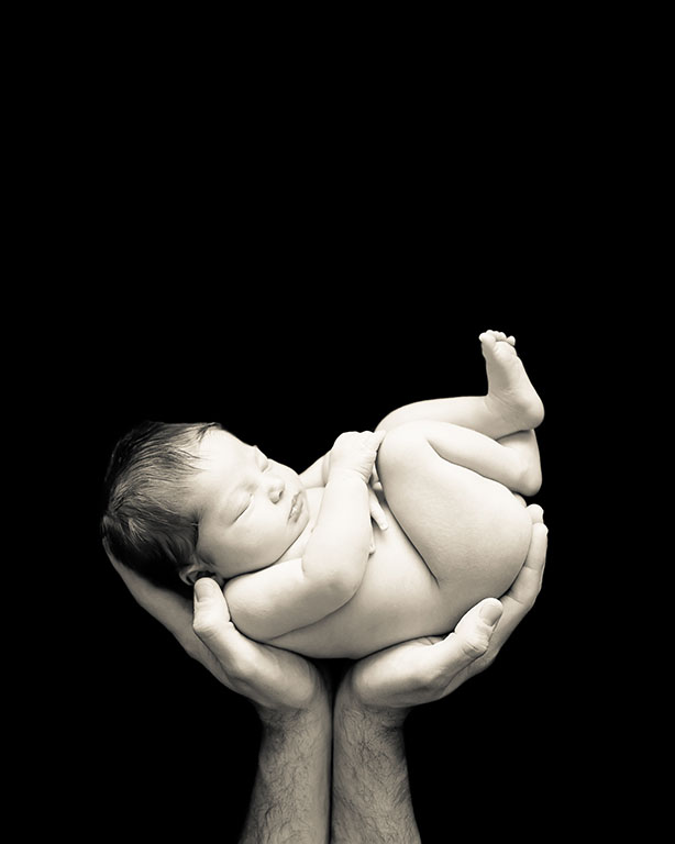 Newborn held in the hands of her father.