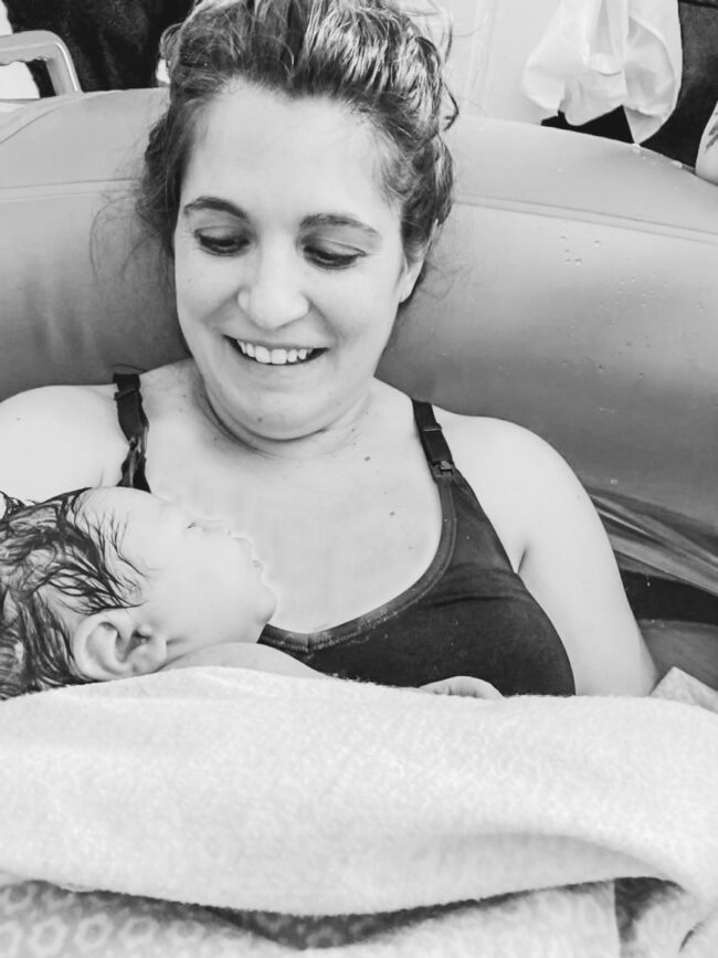 The author smiling while holding her newborn daughter in the birthing tub